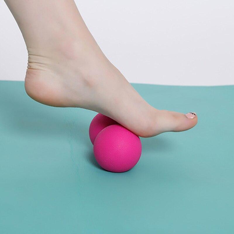 Foot pressing on a pink peanut massage ball for muscle relief on a blue exercise mat.